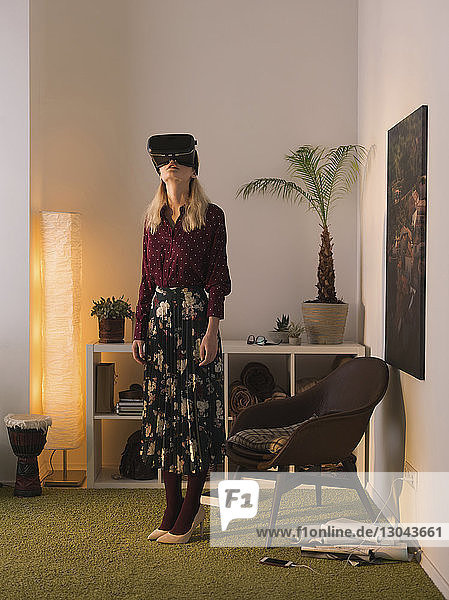 Eine Frau in voller Länge benutzt einen Virtual-Reality-Simulator  während sie zu Hause an der Wand steht