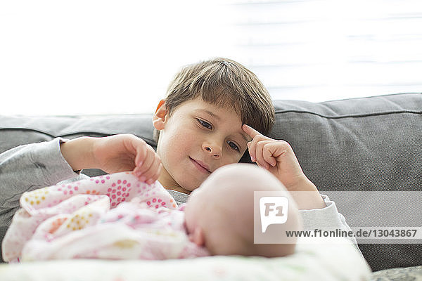 Brother looking at newborn sister on sofa at home