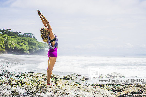 Seitenansicht einer fitten Frau  die Yoga auf Felsen am Strand gegen den Himmel macht