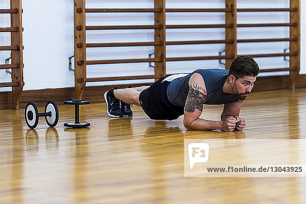 In voller Länge muskulös tätowierter Sportler  der auf einem Holzboden in einer Turnhalle eine Plankenübung macht