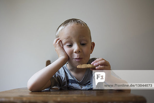 Cute boy looking at cookie while sitting against wall at home