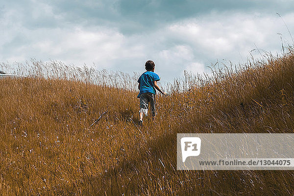 Rear view of boy climbing hill against cloudy sky