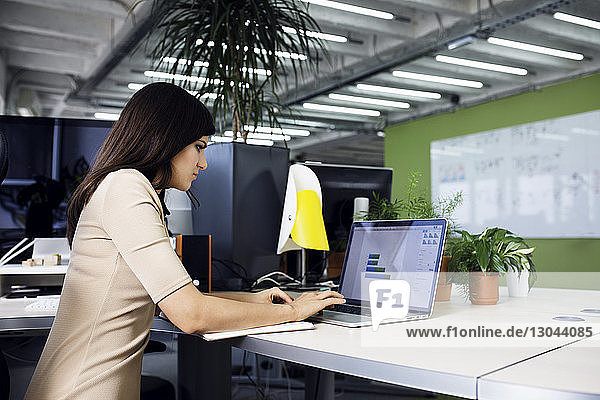 Side view of businesswoman using laptop at desk in creative office