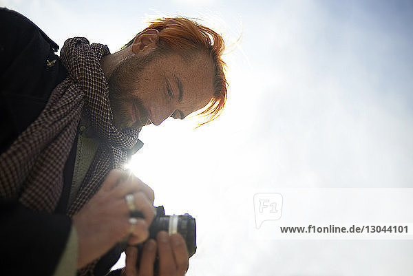 Low angle view of man watching pictures on DSLR camera against sky