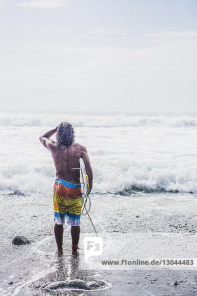 Rückansicht eines männlichen Surfer  der ein Surfbrett trägt  während er am Ufer steht