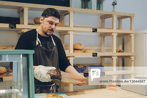 Bäckereibesitzer verpackt Brot in Papiertüte  während er am Tresen steht