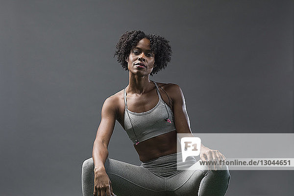 Porträt einer selbstbewussten Frau in Sportkleidung  die im Fitnessstudio an der Wand sitzt