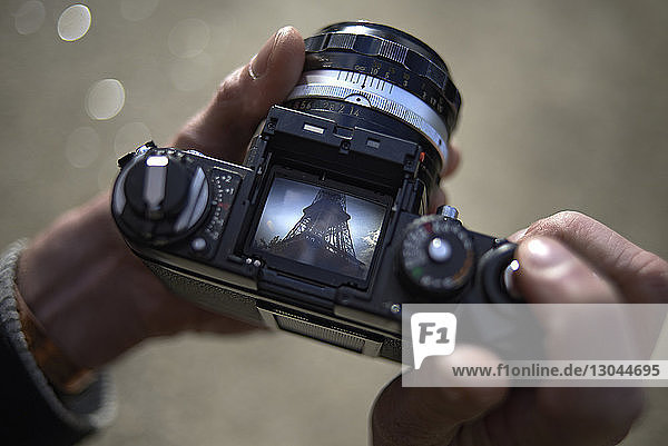 Ausschnitt eines männlichen Touristen  der eine DSLR-Kamera hält und das Bild des Eiffelturms zeigt