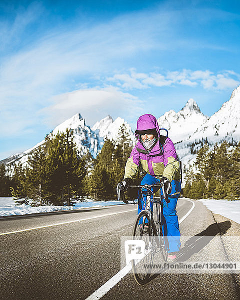 Frau in voller Länge mit dem Fahrrad auf der Straße gegen schneebedeckte Berge im Grand-Teton-Nationalpark