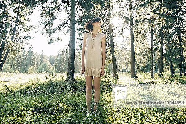 Full length of young woman standing on grassy field in forest
