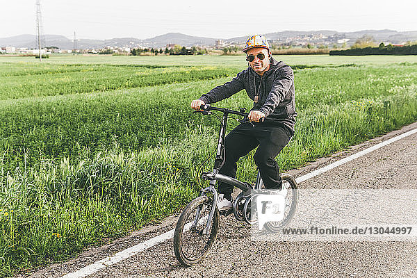 Porträt eines Fahrrad fahrenden Mannes auf Straße durch Bauernhof gegen Himmel