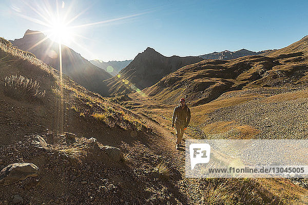 Hiker walking on dirt road against blue sky