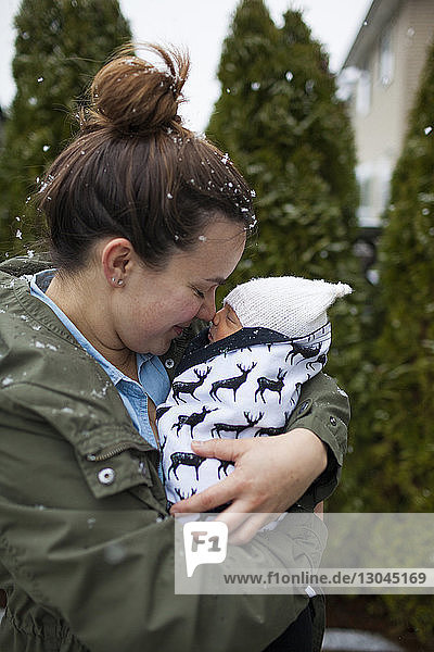 Mother rubbing noses with baby boy while carrying him at yard