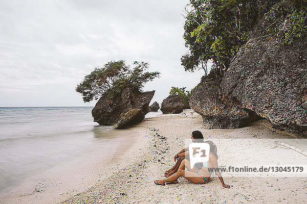 Seitenansicht eines Paares  das an Felsen am Ufer sitzt