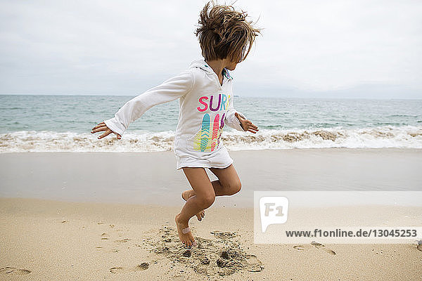 Verspieltes Mädchen schaut weg  während es am Seal Beach gegen den klaren Himmel springt