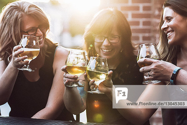 Fröhliche Freundinnen stoßen bei sonnigem Wetter Bier an  während sie im Straßencafé sitzen