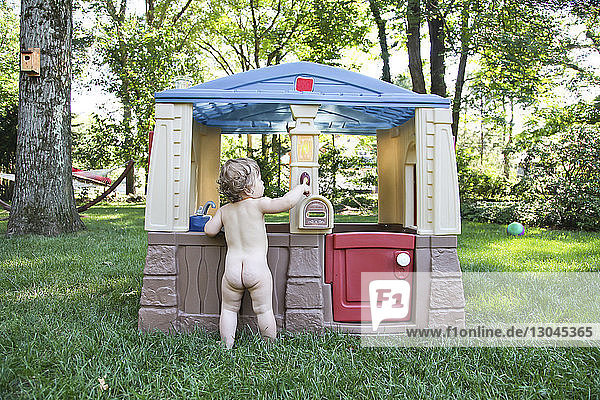 Rückansicht eines nackten Kleinkindes am Spielhaus im Park
