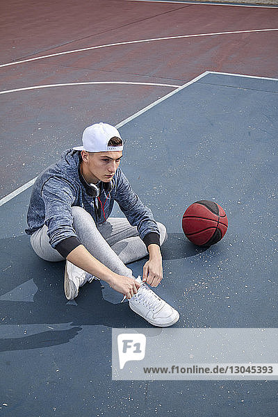 Schrägansicht eines Teenagers  der am Basketballplatz sitzt und sich die Schnürsenkel bindet