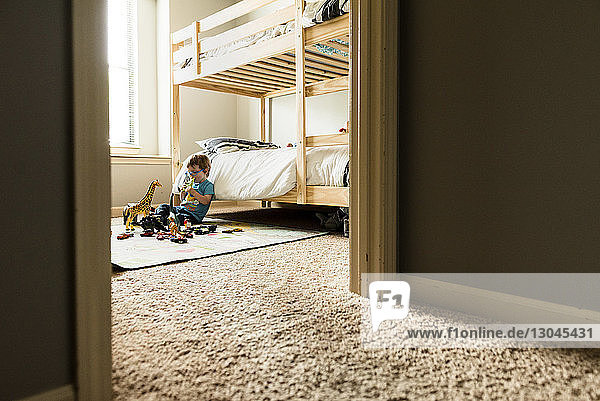 Junge spielt mit Spielzeug im Schlafzimmer mit Blick durch die Tür