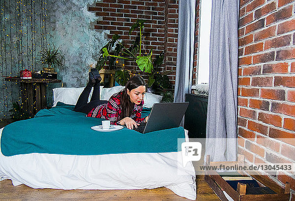 Frau benutzt Laptop-Computer  während sie sich zu Hause im Bett entspannt