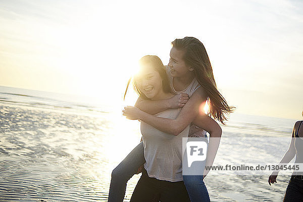 Glückliche Teenagerin mit Huckepack-Freundin am Strand