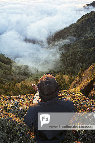Hochwinkelansicht eines Wanderers  der auf dem Gipfel eines Berges sitzt und auf die Aussicht schaut
