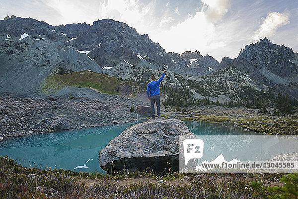 Rear view of hiker holding cap while standing on rock by lake against mountains at Olympic National Park