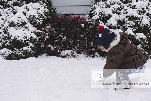 Side view of girl playing with snow in backyard