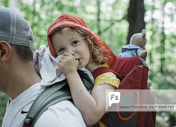 Porträt einer süßen glücklichen Tochter  die am Daumen lutscht  während sie vom Vater im Wald getragen wird