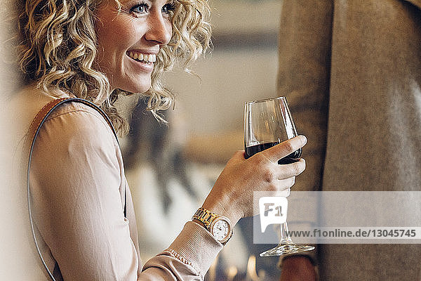 Fröhliche Geschäftsfrau hält Weinglas in der Hand  während sie im Hotel wegschaut