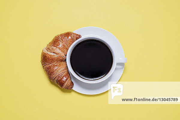 Draufsicht auf schwarzen Kaffee und Croissant auf gelbem Tisch