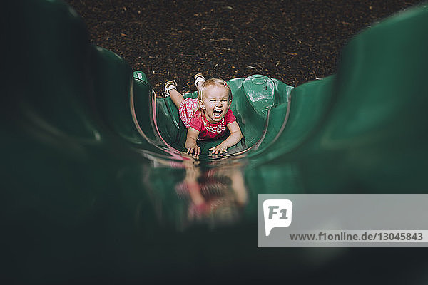 Hochwinkelporträt eines glücklichen Mädchens  das auf einer Rutsche auf einem Spielplatz spielt