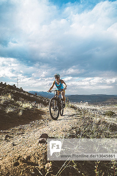 Female cyclist riding bicycle on semi-arid landscape against cloudy sky