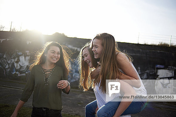 Teenagerin schaut Freunden bei Sonnenschein beim Huckepacktragen zu
