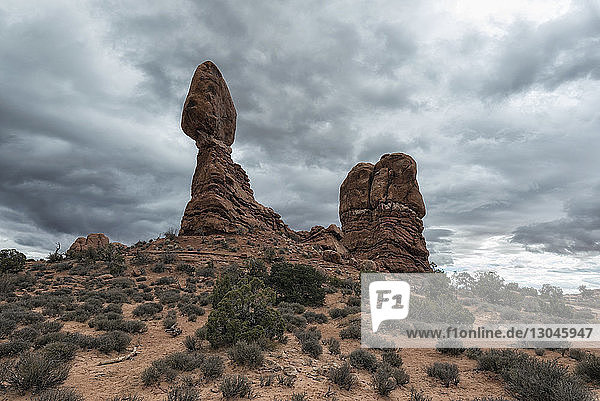Low angle view of rock formations on field against cloudscape