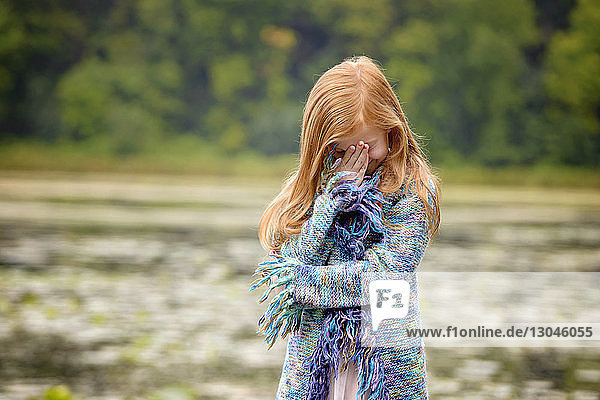 Mädchen versteckt Gesicht mit der Hand  während sie am See steht