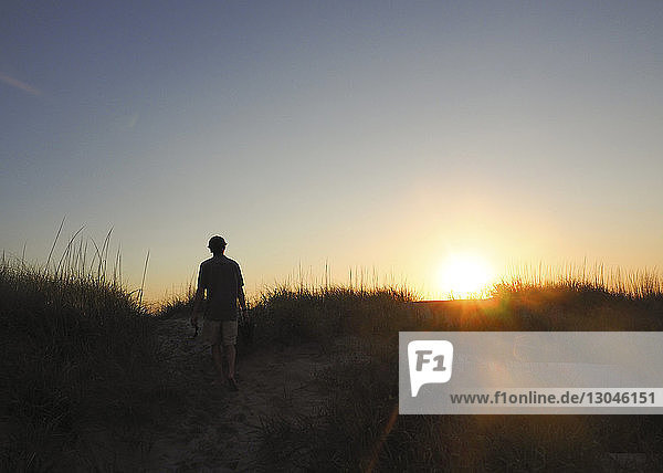 Rear view of hiker walking on field at Nags Head against clear sky during sunset
