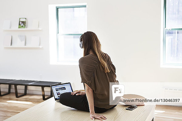 Rear view of businesswoman using laptop while sitting on desk in creative office