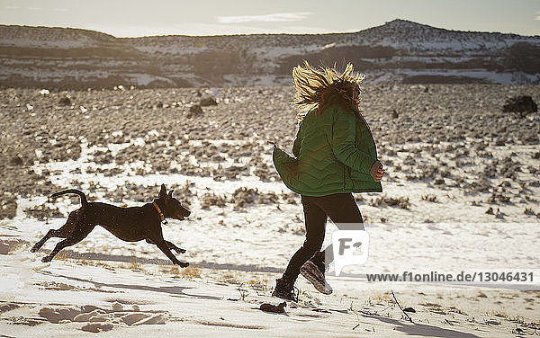 Happy woman playing with dog on snow covered field