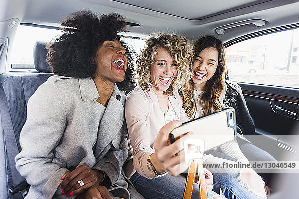 Fröhliche Geschäftsfrauen beim Selbstfahren mit Smartphone im Auto