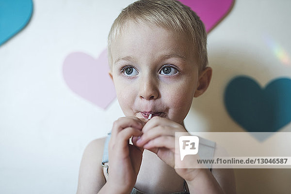 Cute boy looking away while sucking lollypop at home