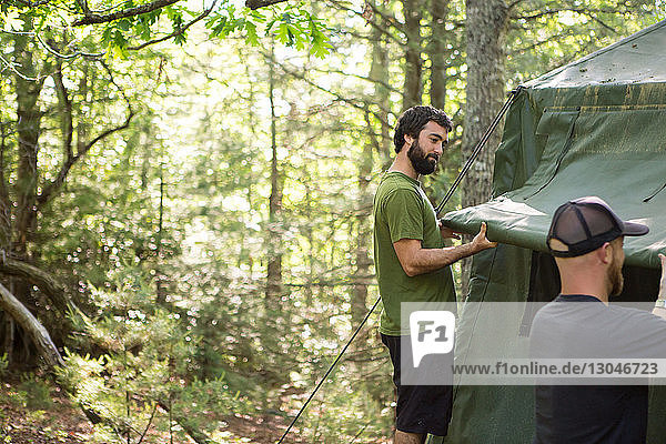 Male hikers making tent at campsite in forest