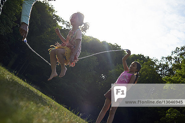 Mutter und Töchter spielen im Sommer im Park mit dem Springseil