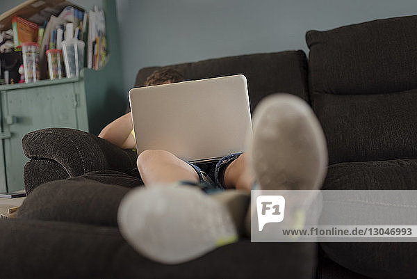 Ein Junge in voller Länge benutzt einen Laptop-Computer  während er sich zu Hause auf dem Sofa entspannt