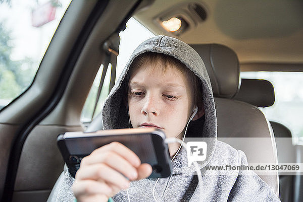 Boy wearing hooded shirt using smart phone while sitting in car