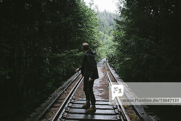 Side view of man looking over shoulder on railway tracks amidst trees