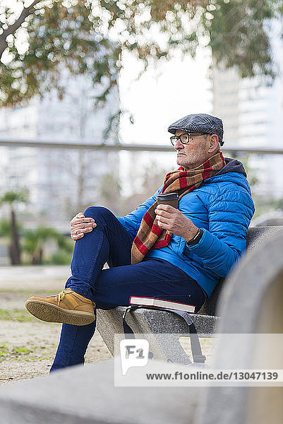 Nachdenklicher Mann mit Kaffee und Buch auf Parkbank sitzend