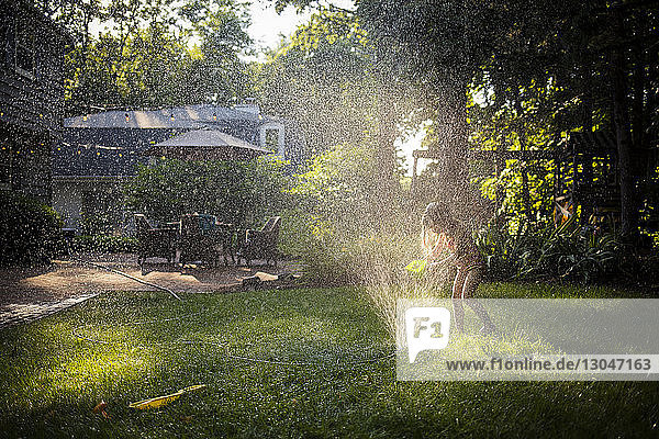 Happy girl in swimwear playing with sprinkler in backyard