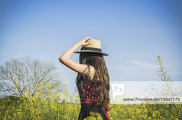 Seitenansicht eines Teenager-Mädchens mit Hut  das bei sonnigem Tag auf dem Feld vor blauem Himmel steht