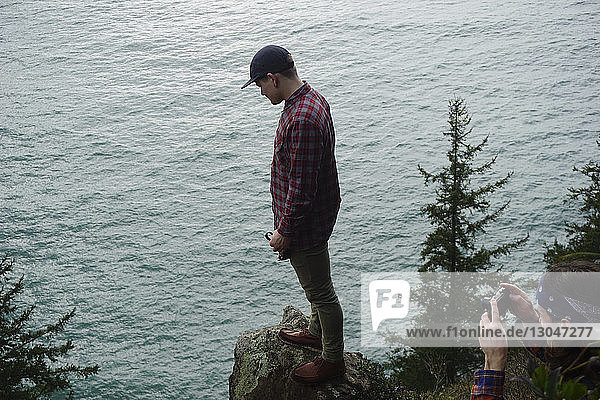 Hochwinkelaufnahme eines Mannes  der einen Freund fotografiert  der auf einem Felsen am Meer steht